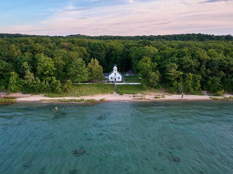 drone view from water looking back at front of Mission Point Lighthouse