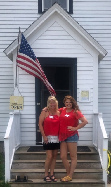 Mother and daughter lighthouse keepers standing on front steps with flag