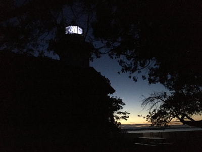 night time view of lighthouse silhouette against dusk sky with light in tower 